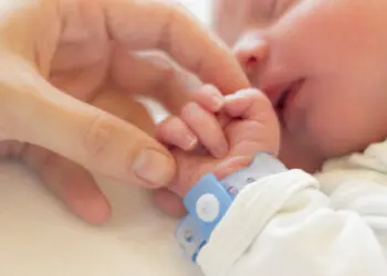 Newborn baby boy sleeping in his crib, his mother's hand holding his little hand.